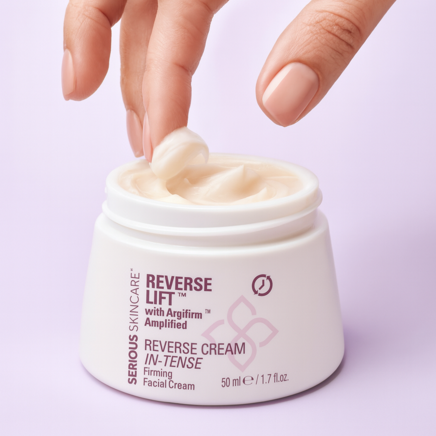 A close-up of a hand with manicured nails reaching into an open white jar of Serious Skincare Reverse Lift Reverse Cream In-Tense facial cream, showing the creamy product texture, against a solid light lavender background.