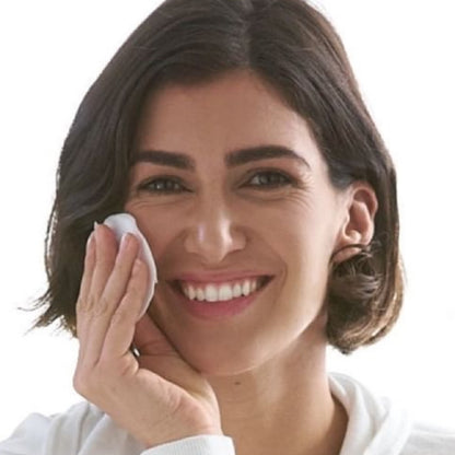 Woman cleaning her face with a white cloth against a plain background