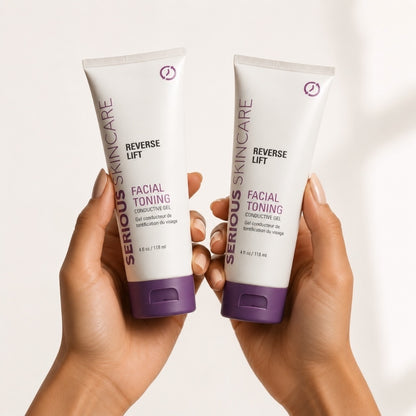Two hands holding two white tubes of Serious Skincare Reverse Lift Facial Toning Conductive Gel against a clean white background.