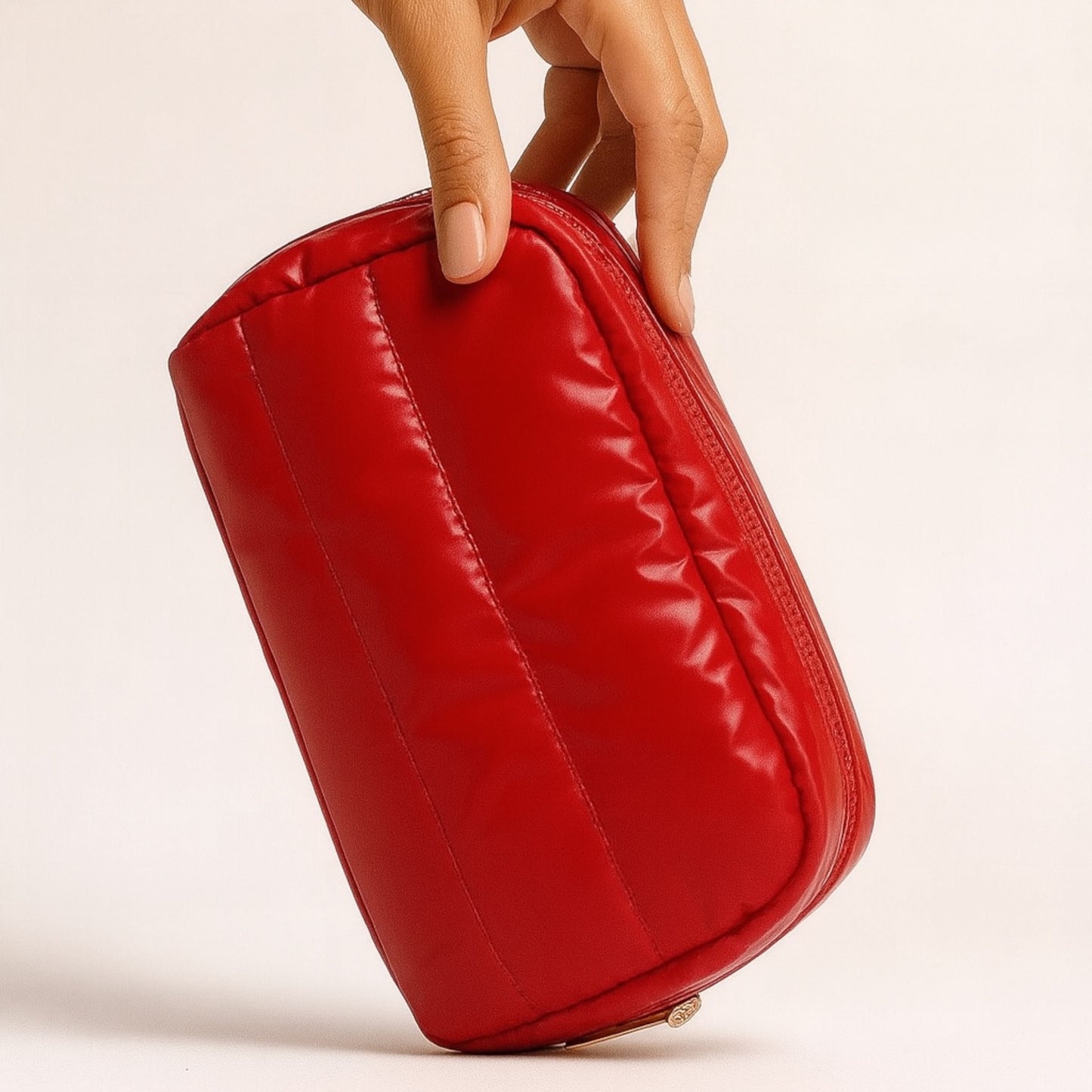 Red puffy pouch held by a hand on a beige background